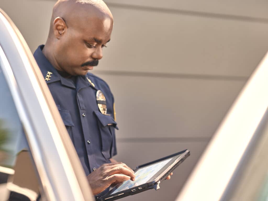 Male police office holding a Surface Go 3 in a ruggedized case with Teams calendar screen shown.