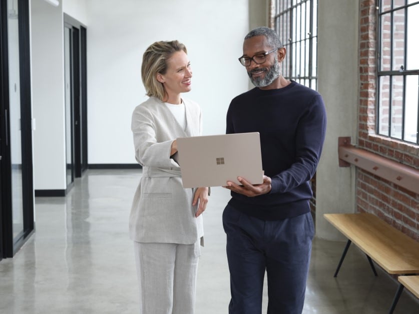 Man and woman standing in an office hallway discussing content on a laptop.