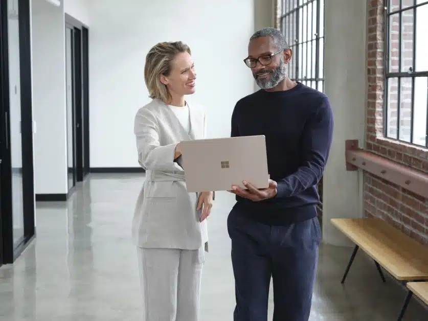 Man and woman standing in an office hallway discussing content on a laptop.