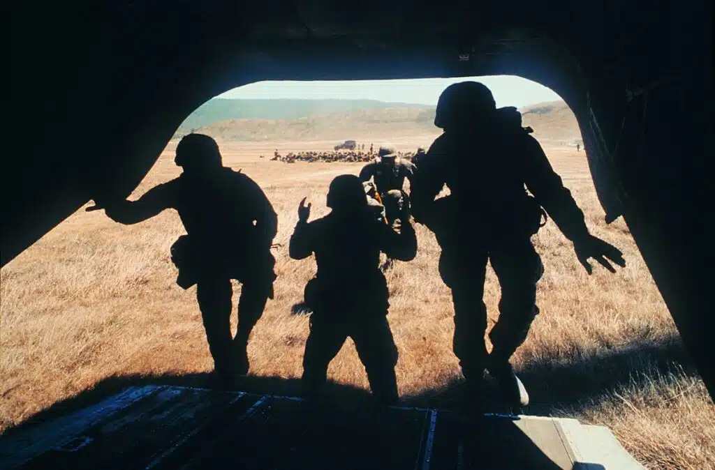 Image of defense personnel boarding the back of plane in a remote area, with troops and vehicles in the background.