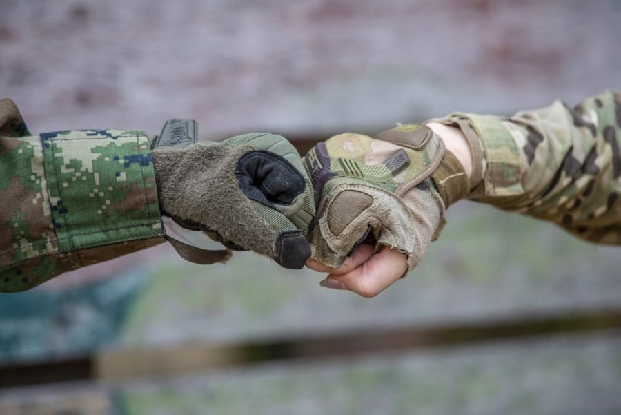 Two hands first bumping from two people offscreen wearing military camo.