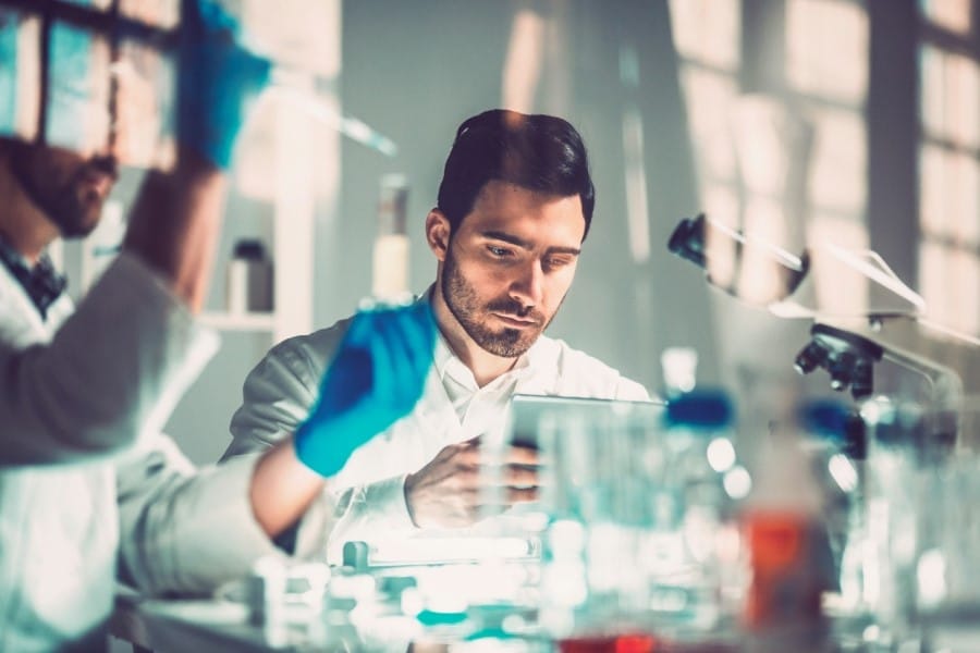 Man sitting in a research laboratory environment, reviewing data on a tablet.