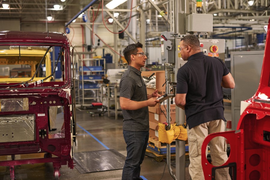 Two engineers wearing safety goggles use machinery at a manufacturing plant.