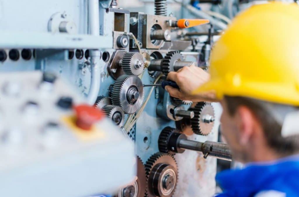 Person wearing yellow hard hat fixing cogs in a machine