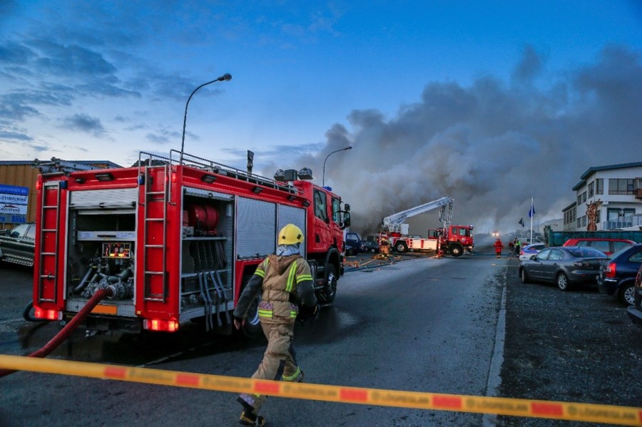 Emergency response personnel in gear running towards a fire in a roped off area in a residential community with one fire truck in the forefront and one firetruck in the background