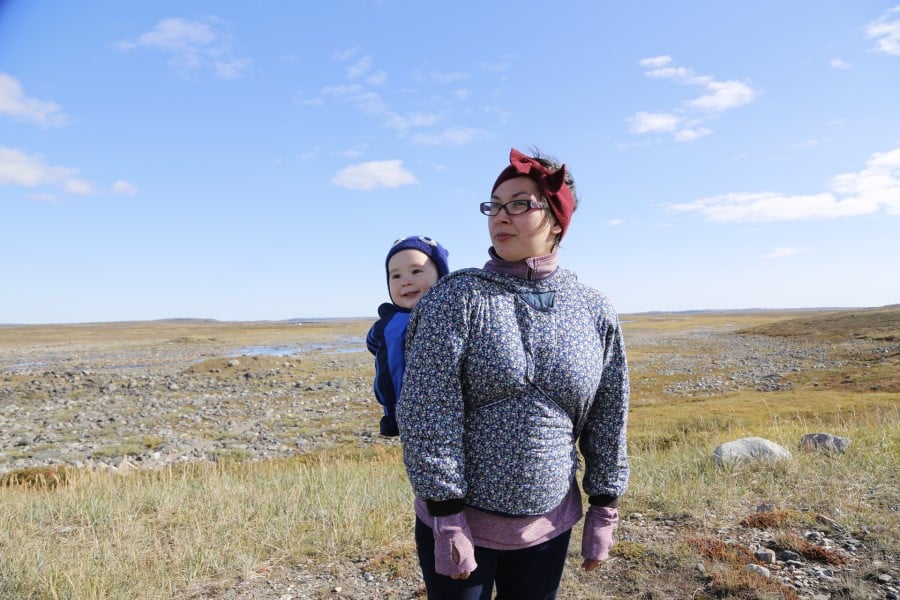 Woman wearing baby on back standing in an open field in Canada.