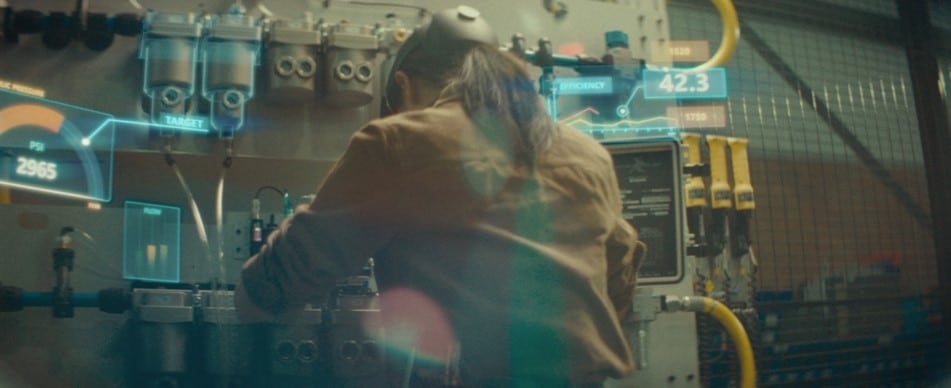 A woman is engaged in deep work in front of a tall machine. Around her are holographic infographics displaying the relevant data she needs to reference. 