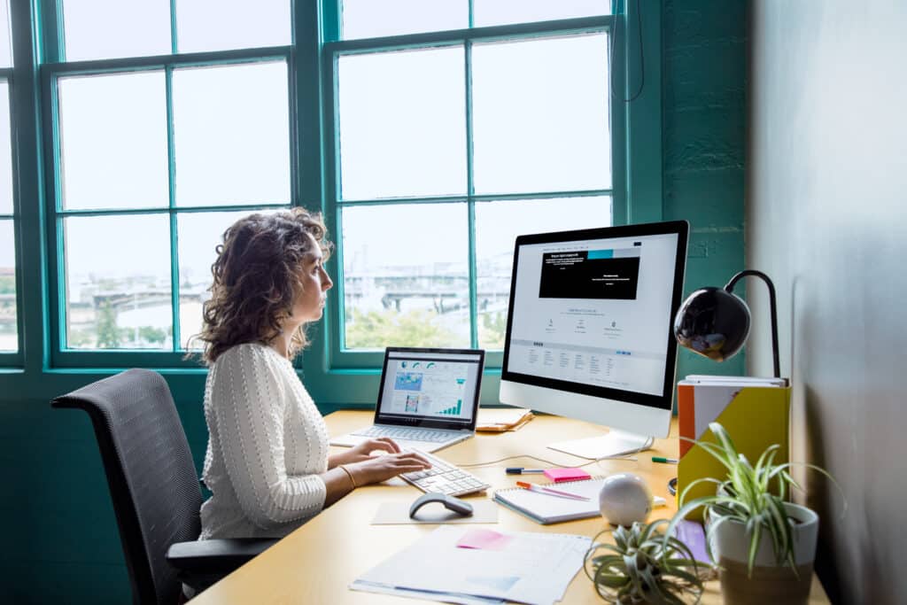 A woman sitting in an office working at a computer near the window.