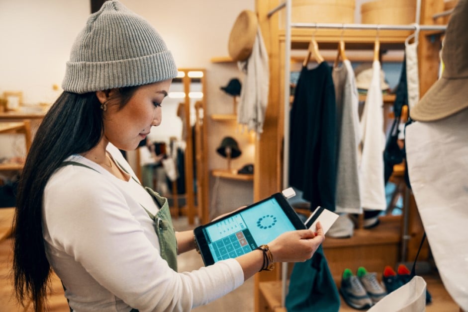 Shop clerk in a clothing boutique taking a credit card payment on a digital tablet.