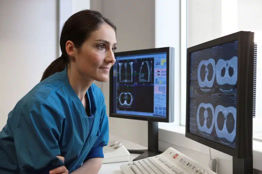 A woman in blue scrubs looking at computer screens