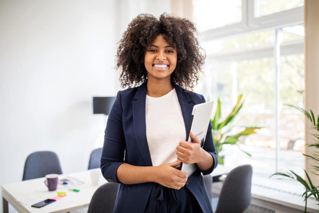 A woman wearing a white t-shirt and blue blazer holding a laptop.