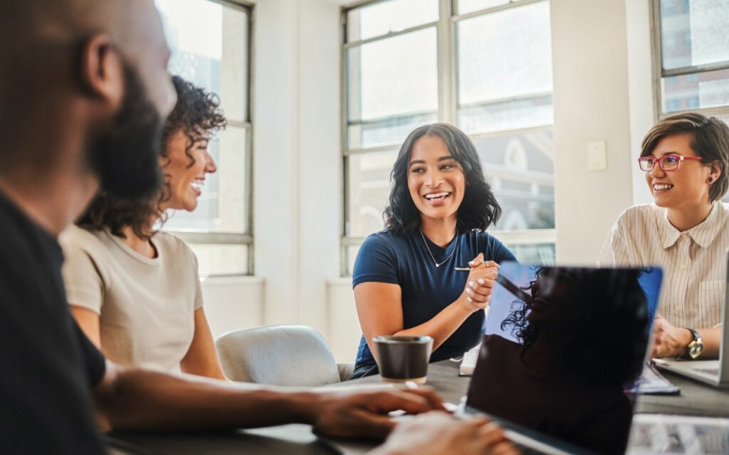 A diverse group of coworkers collaborate in an office space while one takes notes on his laptop.